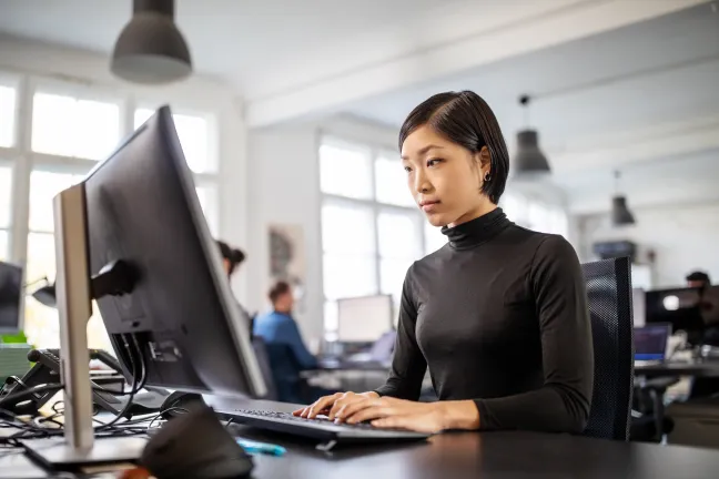 Woman sitting in front of computer screen typing on keyboard